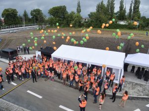 Fotografia z podnośnika na grupę uczestników uroczystości na moment po wypuszczeniu w niebo balonów, które dopiero co uniosły się nad ich głowami.