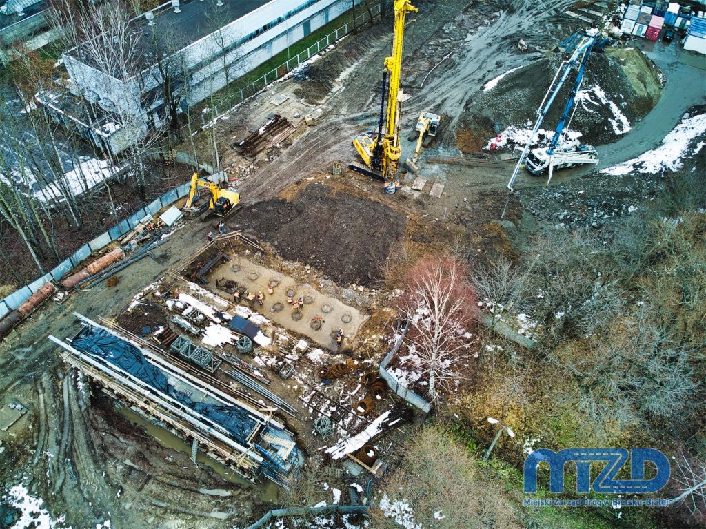 Widok z drona na powstające podpory przyszłego wiaduktu. Przy fundamentach jednej z nich pracuje ekipa budowlana. Obok trwa wiercenie otworów pod kolejne kolejną konstrukcję fundamentów.