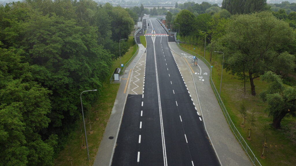 Widok z góry na nową drogę wśród drzew, z oznaczeniami, ścieżkami rowerowymi, przystankami i chodnikami.