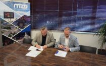 Dyrektor MZD Patryk Owcarz i Mateusz Kurtok, Prezes firmy RADEX, podpisują dokumenty przy stole konferencyjnym. Za nimi stoi baner MZD z fotografiami infrastruktury drogowej.